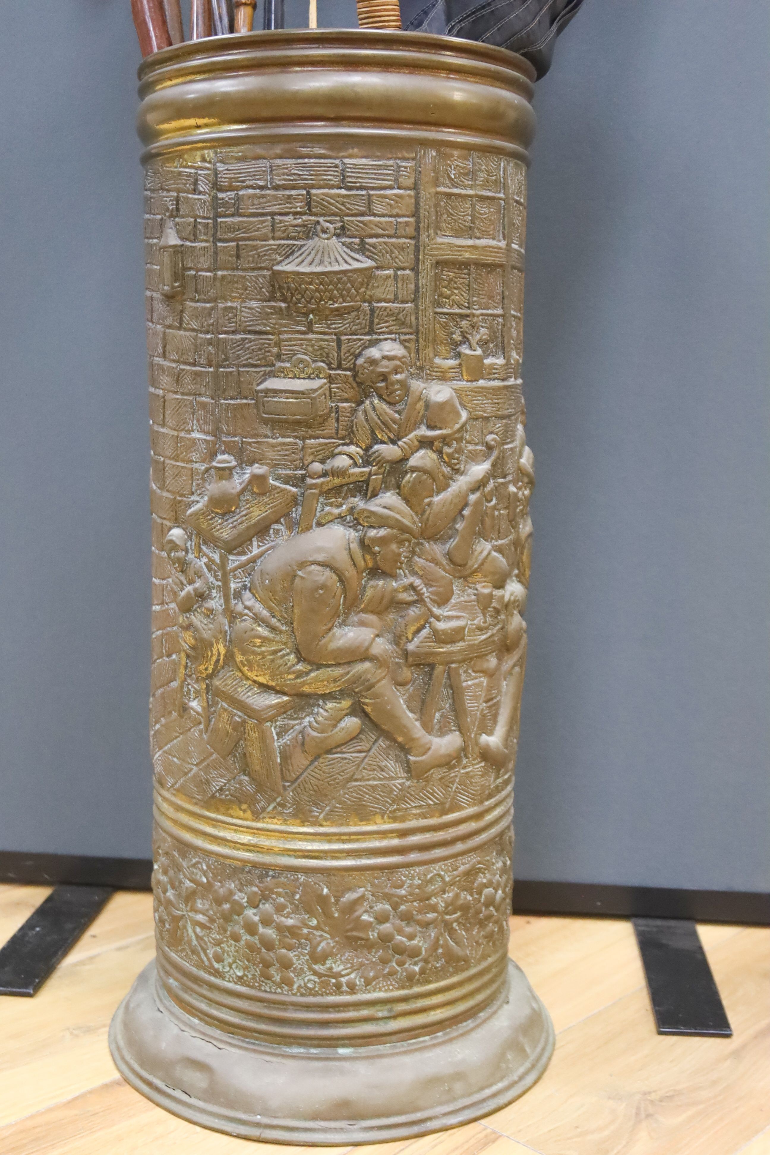 A cylindrical repousse brass stick stand, with walking sticks, parasols, etc.